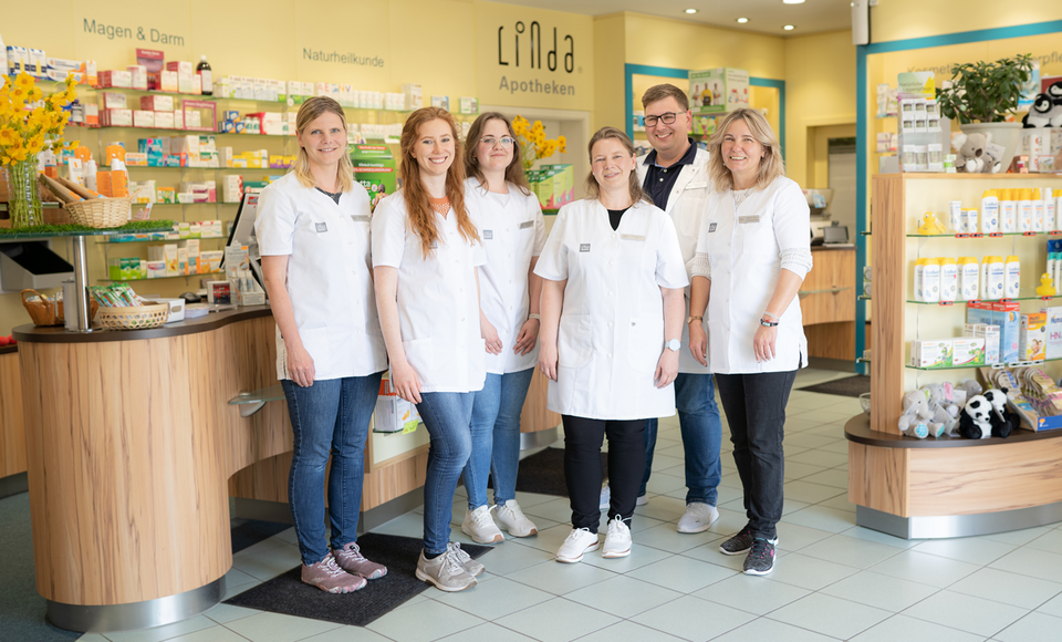 Lächelndes Apothekenteam steht vor den Kassen mittig im Verkaufsraum.